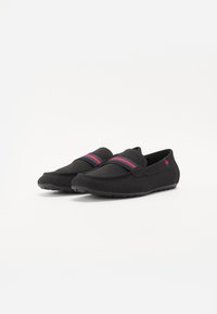 Sorte slip-on sko laget av mykt stoff, med en tettsittende design, en fargerik rød- og blåstripet detalj foran og en teksturert såle.