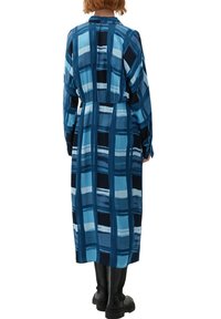 Blaues langärmliges Kleid mit einem Karomuster in verschiedenen Blau- und Schwarztönen. Es hat eine geraffte Taille und eine fließende Silhouette.