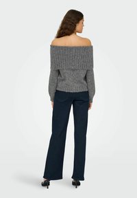 Pull gris à épaules dénudées avec texture côtelée, associé à un jean droit noir et des talons noirs. Design simple et décontracté.
