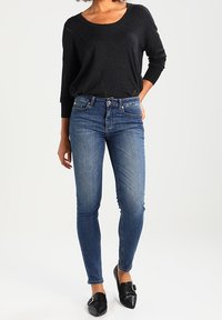 Top ligero de manga larga en gris oscuro con escote redondeado, combinado con jeans ajustados azules. Textura de denim suave, corte hasta el tobillo y mocasines negros.