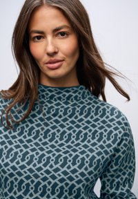 Maglione ceruleo con motivo a geometria presenta un design in azzurro chiaro. Texture morbida con linee e forme distintive.
