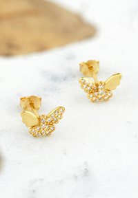 Guld fjärilsstick-on örhängen med kristallaccenter, som har texturerade vingar och en polerad yta. Liten storlek, intrikata detaljer förbättrar designen.