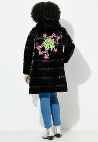 Cappotto imbottito lucido nero con un design grafico verde e rosa di stelle e testo sul retro. Ha un cappuccio e cuciture voluminosi.