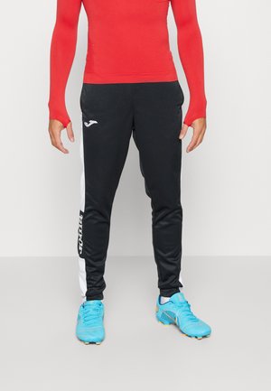 Pantalons de sport noirs avec des rayures blanches sur les côtés, arborant un logo sur la cuisse gauche. Assortis avec des baskets de sport bleu vif.