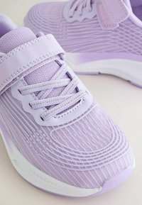 Chaussures de sport lilas en tissu mesh, lacets et fermetures à bandes auto-agrippantes, semelles blanches rembourrées.