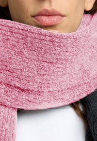Rosa stickad halsduk gjord av mjukt, texturerat tyg, hängande runt halsen, med synliga trådar och ett löst vävmönster.