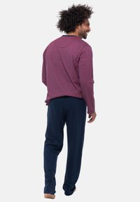 Maglietta a maniche lunghe color bordeaux con una consistenza morbida, abbinata a pantaloni blu scuro. Cuciture visibili e vestibilità rilassata. Design semplice senza motivi.