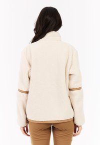 Jaket od flisa boje kreme s visokim ovratnikom, dugim rukavima i smeškastim detaljima. Teksturirana tkanina i opušten fit.