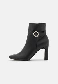 Czarne skórzane botki za kostkę z wąskim noskiem, średniej wysokości obcasem typu stiletto oraz ozdobnym paskiem z okrągłym akcentem perłowym.