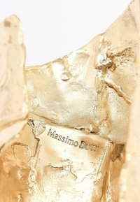 Oggetto decorativo metallico dorato con superficie testurizzata e forma irregolare, con etichetta incisa "Massimo Dutti".