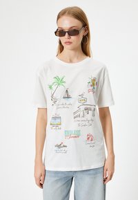 Hvid bomulds t-shirt med farverige sommer-inspirerede grafikker, herunder palmer, drinks og tekst, med korte ærmer og en afslappet pasform.