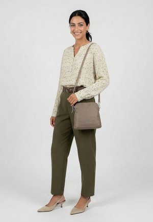 Frau lächelt, trägt eine cremefarbene Bluse mit Struktur, olivgrüne hoch taillierte Hose, beige Slingback-Pumps und hält eine taupefarbene Umhängetasche.