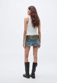 Λευκό αμάνικο τοπ συνδυασμένο με μπλε τζιν μίνι φούστα με χρυσά διακοσμητικά καρφιά. Μαύρες μπότες μέχρι το γόνατο ολοκληρώνουν την εμφάνιση.