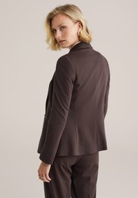 Hnedý prispôsobený blejzer s priliehavým siluetom, ostrými klopami a hladkým materiálom. Pozoruhodné švy a elegantný, minimalistický dizajn.