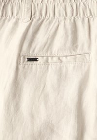 Beige linneshorts med en texturerad tygkonstruktion, elastisk midja och en bakficka med en metallisk accentplatta.