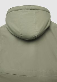 Giacca verde chiaro con cappuccio arrotondato, texture liscia e cuciture semplici. La vista posteriore mostra un design minimale con un dettaglio della cucitura inferiore.