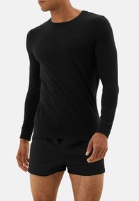 Sort langærmet skjorte lavet af blødt stof, rund hals-design, tætsiddende stil, parret med sorte shorts. Enkel, sømløs konstruktion.
