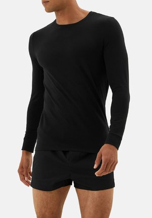 Zwarte langmouwshirt van zachte stof, ronde hals ontwerp, aansluitende stijl, gecombineerd met zwarte shorts. Eenvoudige, naadloze constructie.