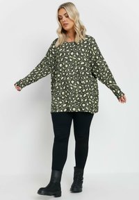 Zielono-oliwkowy sweter w beżowy wzór w panterkę. Posiada długie, luźne rękawy oraz swobodny krój. Zestawiony z czarnymi legginsami i botkami za kostkę.