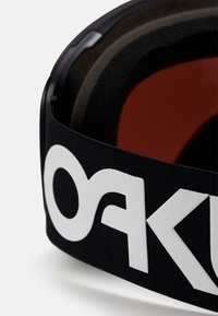 Zwarte elastische band met wit logo, voorzien van een gestructureerd oppervlak en een binnenlaag van donker schuimrubber, met gedeeltelijk zichtbare rode lenzen.