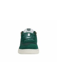 Sneakers in suede verde con accenti in tessuto bianco, caratterizzati da un design con lacci e logo stampato sulla linguetta, e occhielli dorati.