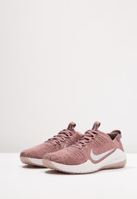 Nike athletic shoes in pink knit material, with silver accents, a textured upper, flat laces, and a white speckled sole.