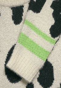 Stickad tröja med en krämfärgad bas och stora svarta prickar. Ärmarna har två gröna ränder. Strukturerat tyg med ribbat manschettdetalj.
