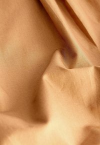 Tissu marron clair avec une texture lisse, présentant de légères plis et replis qui créent des variations subtiles d'ombre et de lumière.