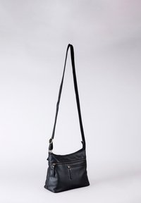 Black leather shoulder bag with a single long strap, featuring multiple zippered compartments and a soft, structured shape.
