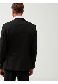 Chaqueta de traje negra a medida, con una única abertura, tela suave, botones brillantes en los puños, solapas afiladas, diseño ajustado, vista desde la parte posterior.