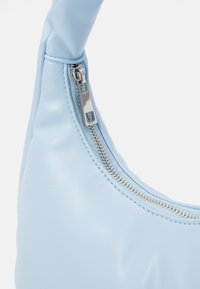 Ljusblå handväska i syntetiskt läder med en böjd form, utrustad med en silverdragkedja och mjuk yta. Utsmyckad med ett mjukt handtag.