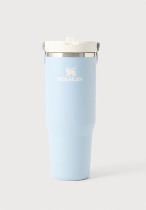 Gobelet isotherme Stanley bleu clair avec couvercle blanc et bord argenté sur un fond clair uni.