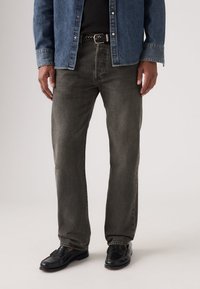 Tumedat halli teksapüksid sirge säärega, kantud musta vöö ja mustade kingadega, seljas sinine teksast nööpidega särk.