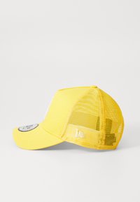 Žltá šiltovka so pevným predným dielom a sieťovinou vzadu, s nakloneným šiltom a logom na boku. Štruktúrovaná tkanina po celom povrchu.