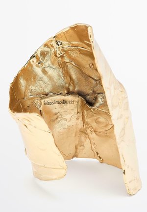 Sculpture abstraite ton or avec une surface texturée, présentant des plis et des froissements. Affiche la marque "Massimo Dutti" à l'intérieur.