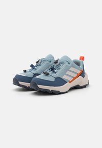 Scarpe sportive azzurro chiaro con tomaia in rete, dettagli blu navy, rifiniture arancioni, suola testurizzata e sistema di laccio a toggle per una vestibilità sicura.