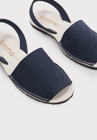 Marineblaue Sandalen mit geschlossenem Zehenbereich und offenem Fersenbereich. Aus Wildleder gefertigt, mit weißen Nähten und einer strukturierten Sohle für besseren Halt.