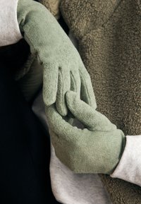 Groene fleece handschoenen met een zachte textuur en gestructureerde vingertoppen, over elkaar heen gedragen, met een subtiele glans en minimale naden.