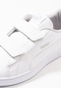 Sneaker bianco con due cinturini in velcro regolabili, tomaia in pelle liscia, fodera in mesh e un sottile logo Puma grigio sul lato.