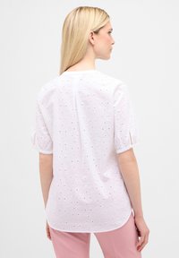 Hvid broderet bluse med korte puffærmer og hulmønsterdetaljer, med en rund udskæring og en buet kant.