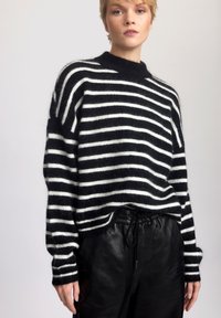 Valkoinen ja musta raidallinen neulepaita, joka on valmistettu pehmeästä ja pörröisestä materiaalista. Siinä on korkea kaulus ja leveät hihat, jotka on yhdistetty mustiin nahkahousuihin.