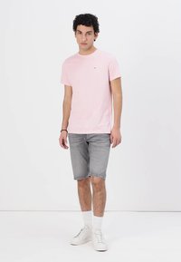 Lys rosa bomull t-skjorte med rund hals, kombinert med grå denimshorts. Modellen har på seg hvite sneakers og sokker i crew-lengde.