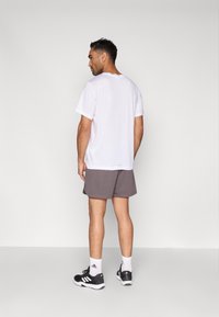 Biała koszulka z krótkim rękawem, szare sportowe spodenki, czarne tenisówki z białymi akcentami, widziane od tyłu. Gładka tkanina, luźny krój.