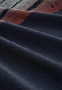 Dunkelblauer Stoff mit subtiler Textur, der rote und cremefarbene horizontale Streifen aufweist. Das Material wirkt weich und leicht elastisch.
