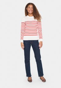 Maglione a maniche lunghe a righe rosse e bianche con scollatura rotonda, abbinato a jeans di denim scuro e ballerine con stampa leopardata. Tessuto dalla consistenza liscia.