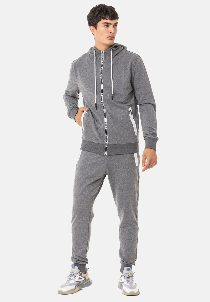 Grau Hoodie- und Jogginganzugset aus weichem Material, mit Reißverschlusstaschen und kontrastierendem Branding am Reißverschluss. Entworfen für maximalen Komfort.