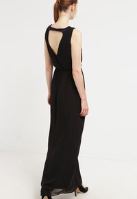 Czarna, bezrękawnikowa sukienka maxi z drapowanym tyłem i detalem w kształcie klucza, wykonana z lekkiego materiału, z dopasowanym pasem i zwiewnym dołem.