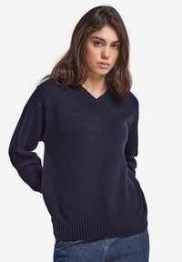 Mörkblå stickad tröja med V-ringning och ribbad fåll. Har långa ärmar och en avslappnad passform, tillverkad av mjukt, strukturerat tyg.