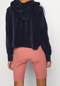 Mörkblå croppad sammetshoodie med huva och vita sidostrippar, kombinerad med rosa ribbade cykelbyxor som når till mitten av låret.