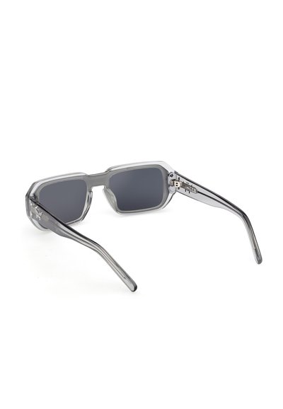 Gafas de sol rectangulares con lentes oscuras, montura gruesa gris translúcida y patillas curvas descansando sobre una superficie blanca.